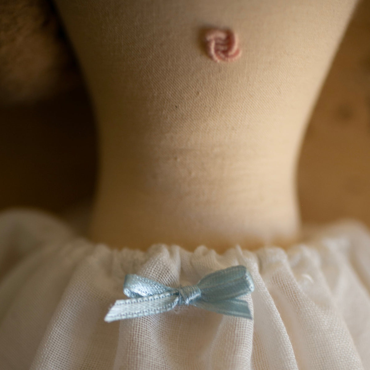 Close-up of a doll wearing a soft white dress with a small light blue ribbon bow at the waist.